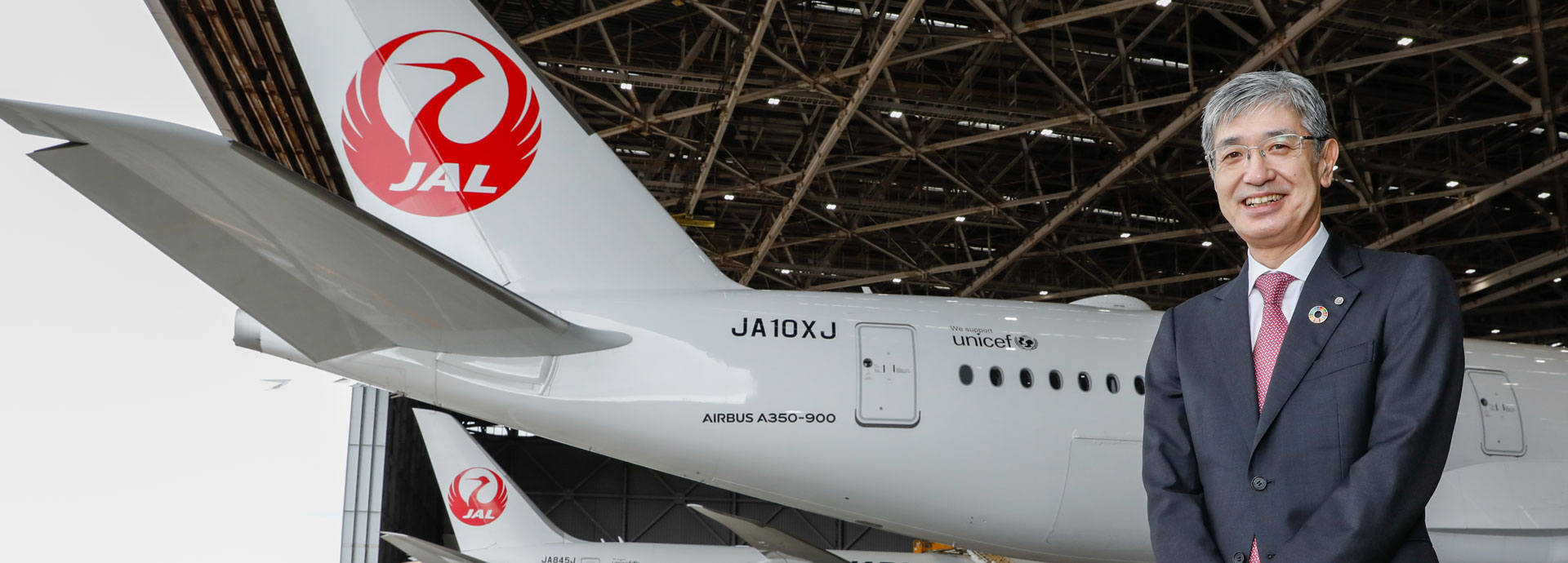 空港内日本航空機を背景とした社長の写真画像