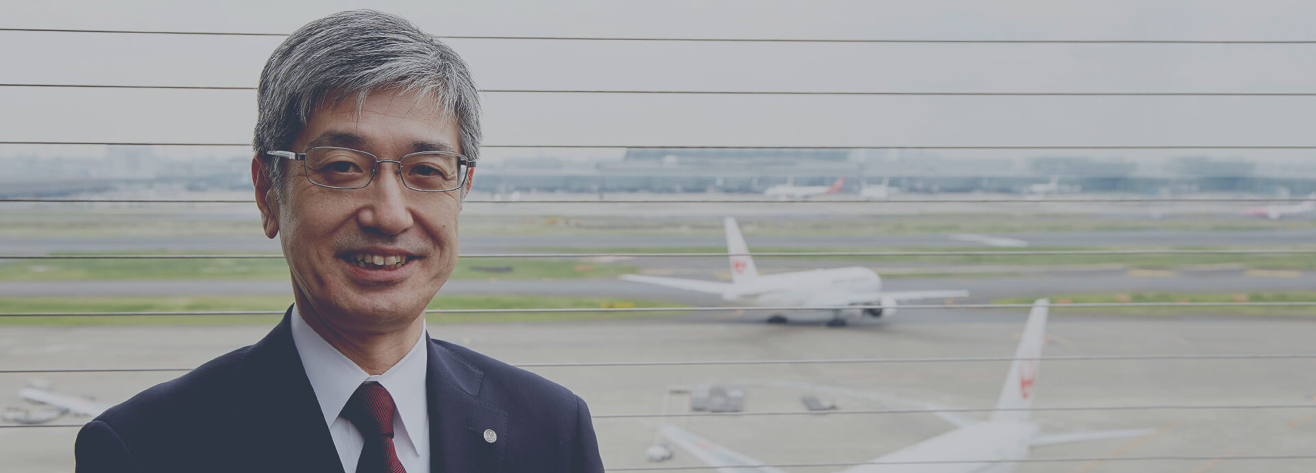 空港内日本航空機を背景とした社長の写真画像