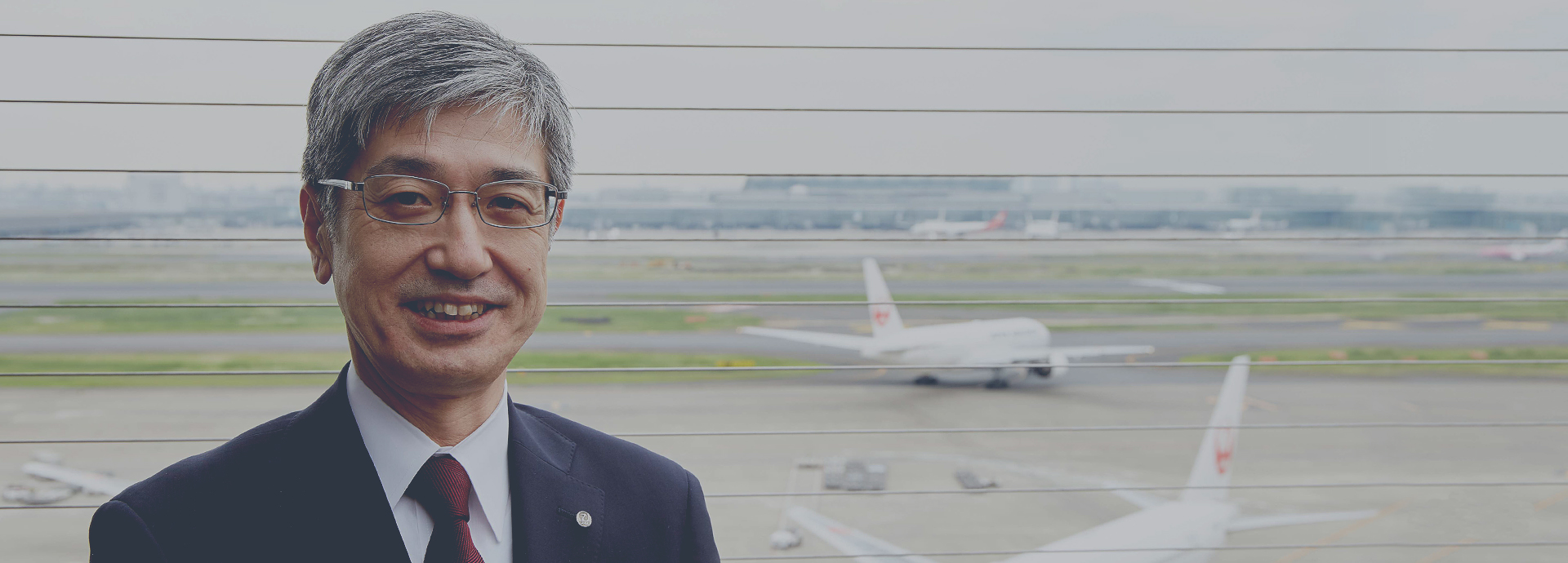 空港内日本航空機を背景とした社長の写真画像
