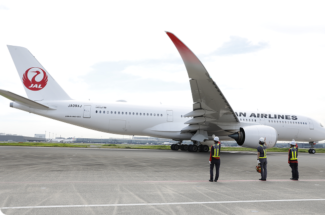 離陸前の飛行機に手を振るグランドハンドリングスタッフたちの後ろ姿