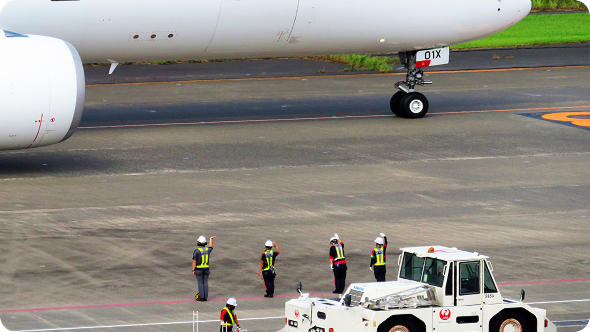 けん引車の横で飛行機に手を振るグランドハンドリングスタッフたち